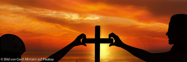 Sonnenuntergang mit Kreuz. Zwei Menschen formen mit Ihren Händen ein Kreuz